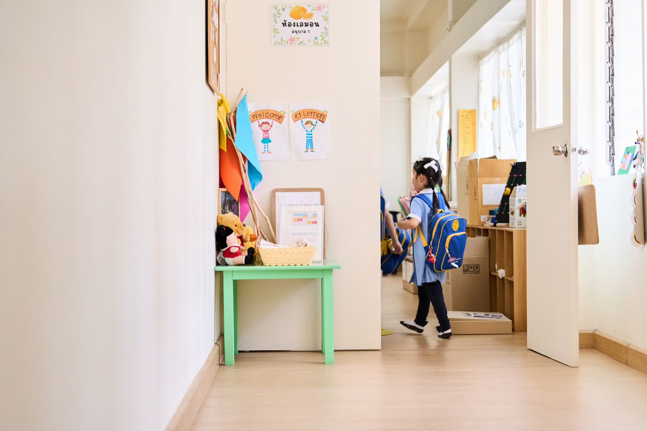 Rear view of little girl with schoolbag entering the classroom at kindergarten